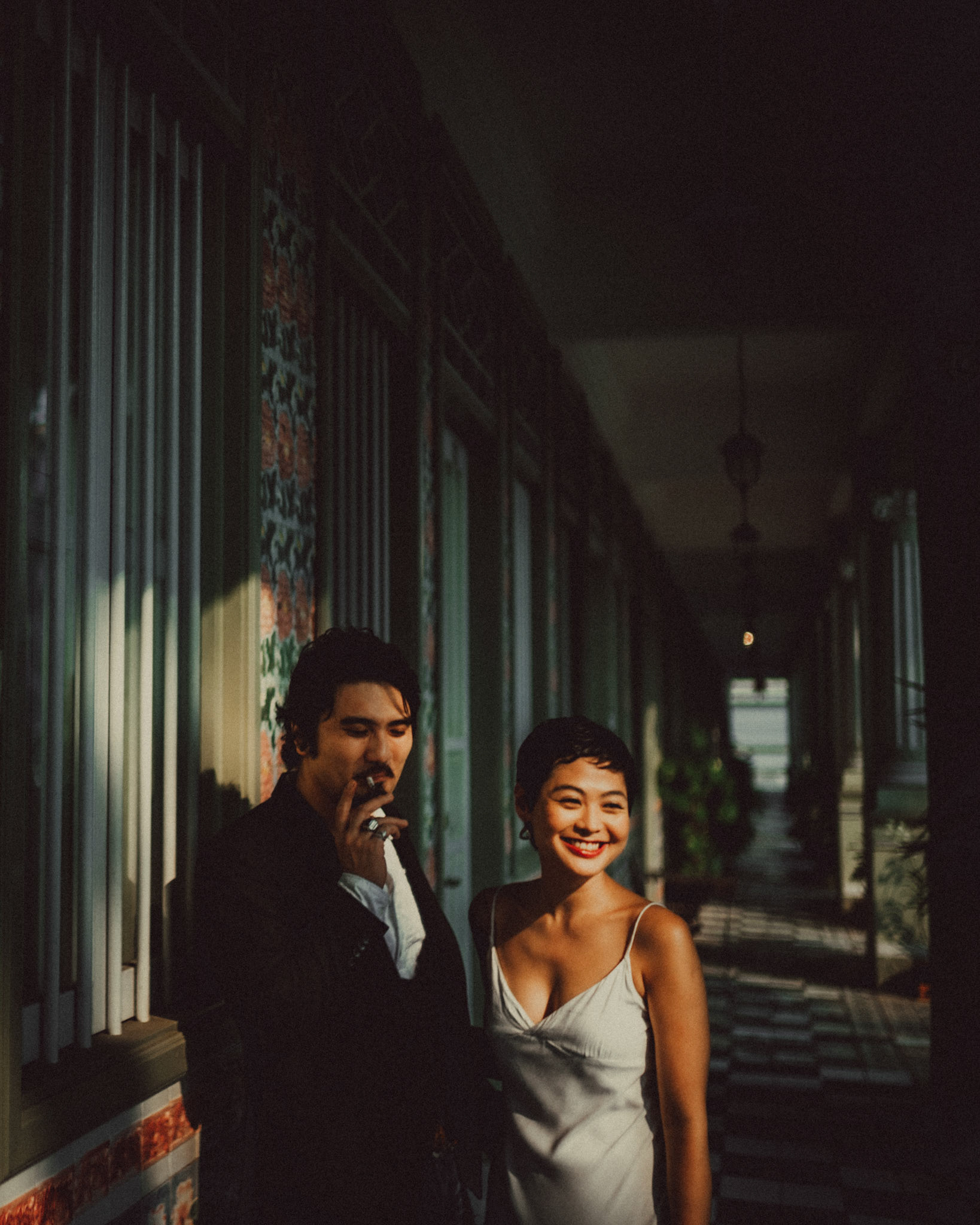 A Japanese couple sharing a lighthearted moment in a sunlit corridor with Peranakan details, from Ibuki and Emi's candid chill engagement shoot, Pertain Road, Little India, Singapore, October 2015, Sony A7S.