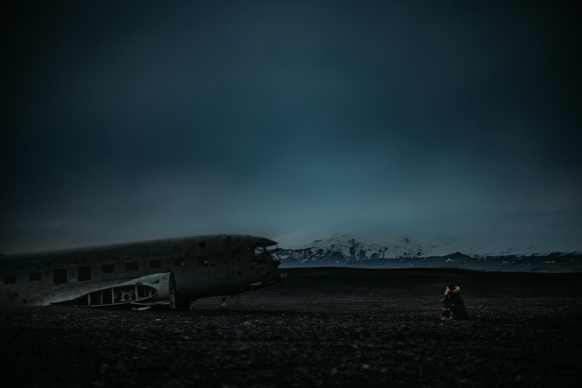 A DC3 plane, a black sand beach, snow capped mountains, a moody blue sky and a tourist in a pensive mood, Solheimasandur, Iceland, May 2016, Sony A7RII.