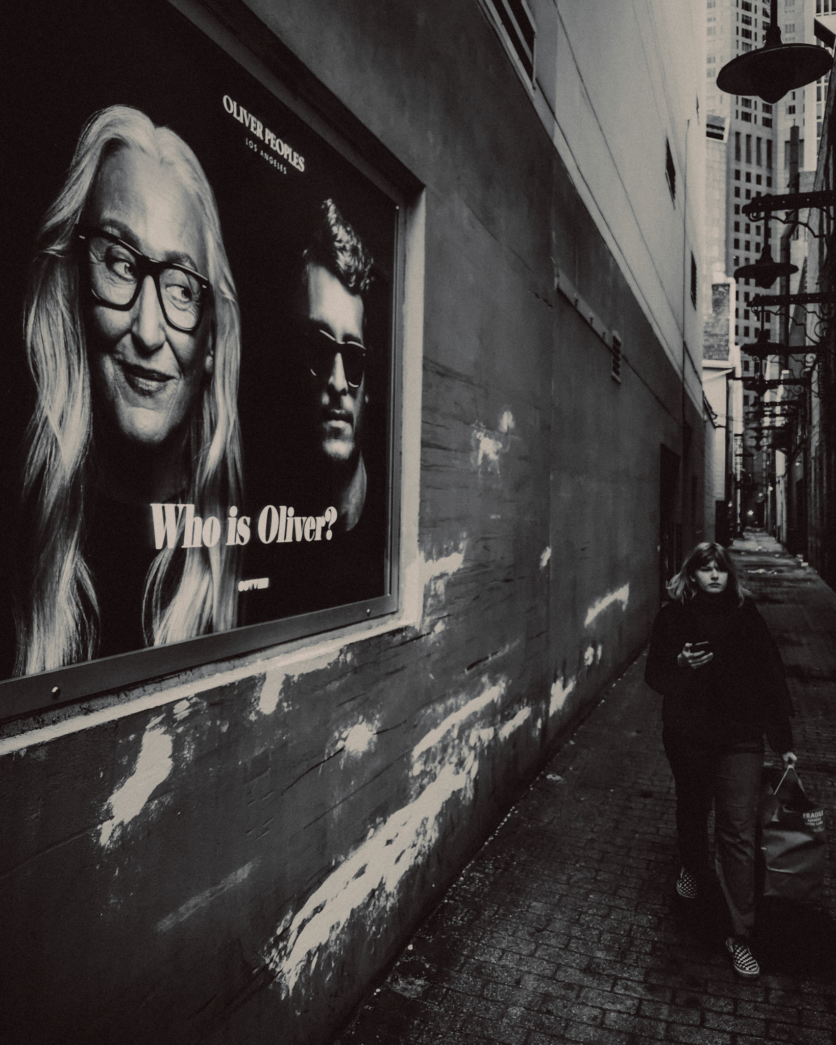 A woman walking past an Oliver Peoples billboard, in black and white, Chicago, Illinois, USA, November 2019, Huawei P30 Pro.
