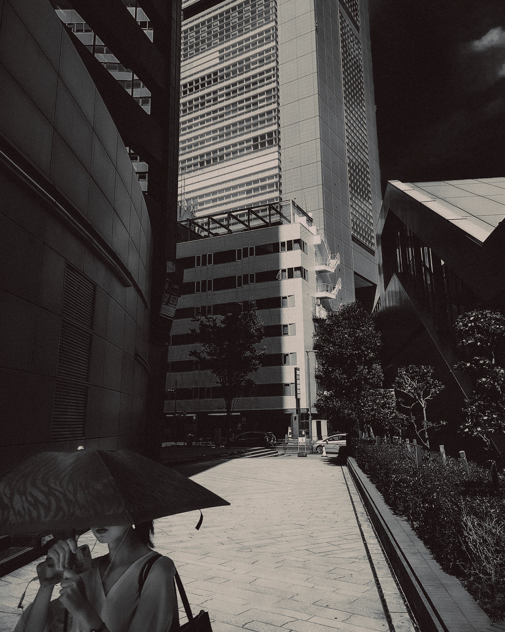 A candid street snapshot of a woman walking with an umbrella covering the upper half of her face, in black and white, Shinjuku, Tokyo, Japan, August 2018, Huawei P20 Pro.