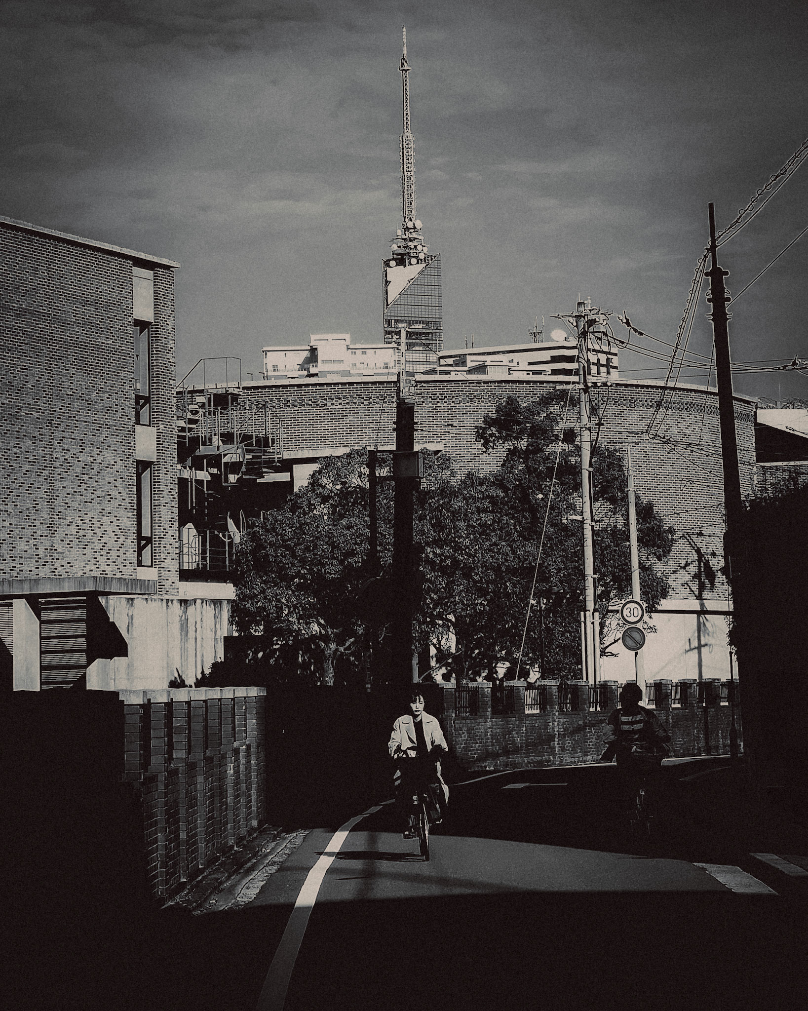 A Japanese woman riding a bicycle with Fukuoka Tower in the background, in black and white, Fukuoka, Japan, October 2018, Huawei P20 Pro.
