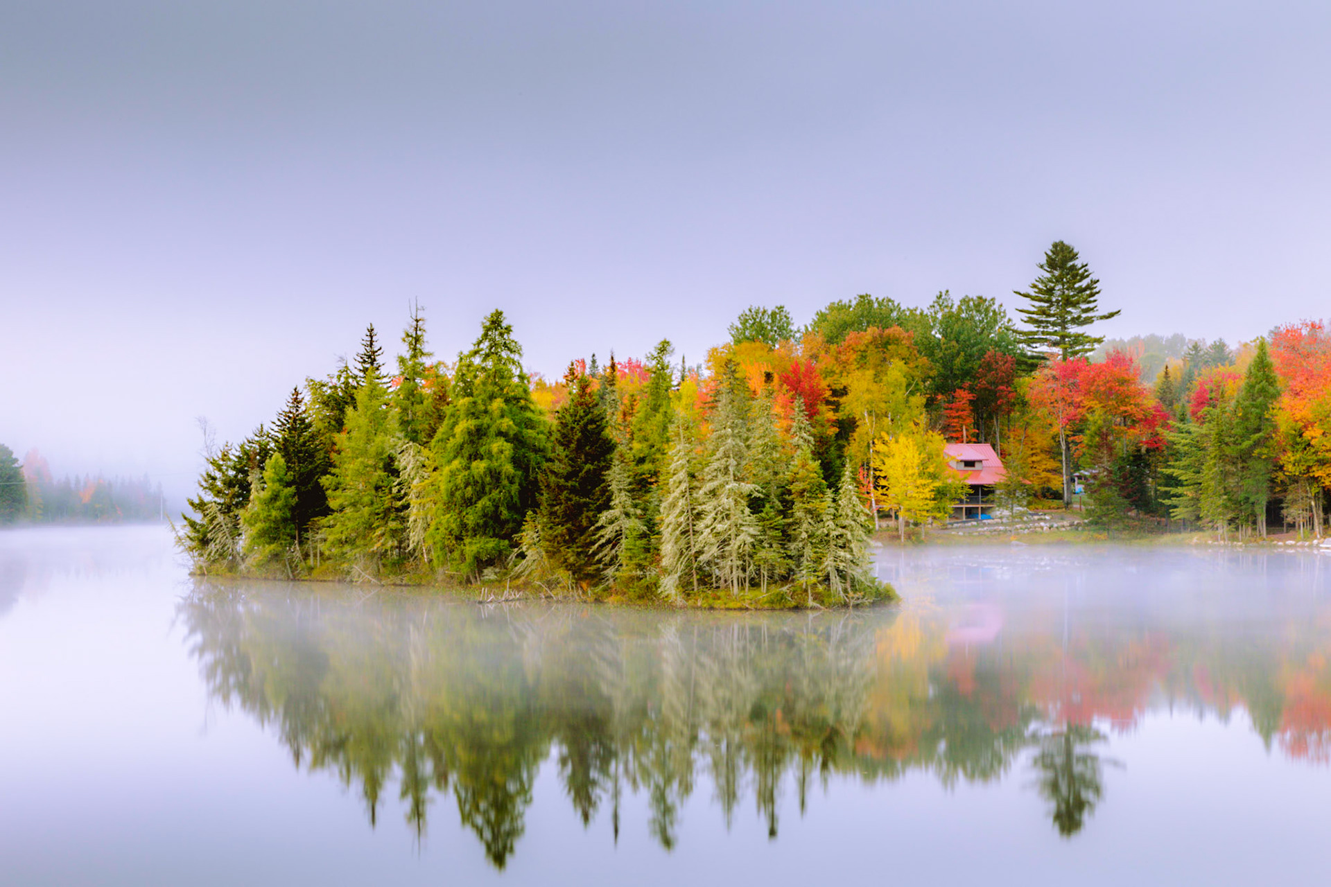 A small island and fog hide a red cabin