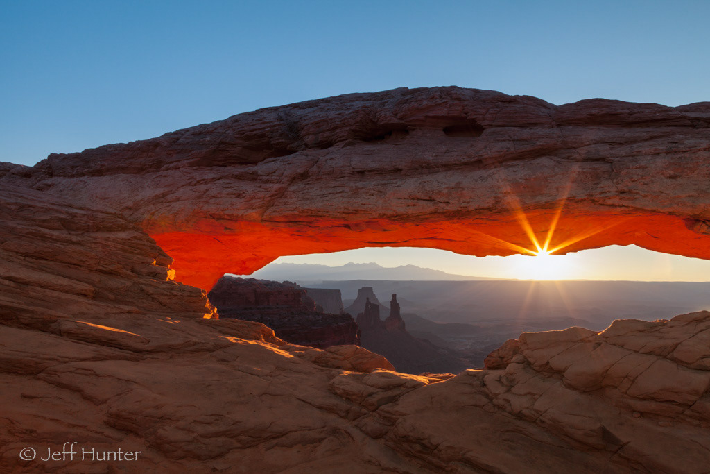 A rock arch with a sunburst coming through at sunrise