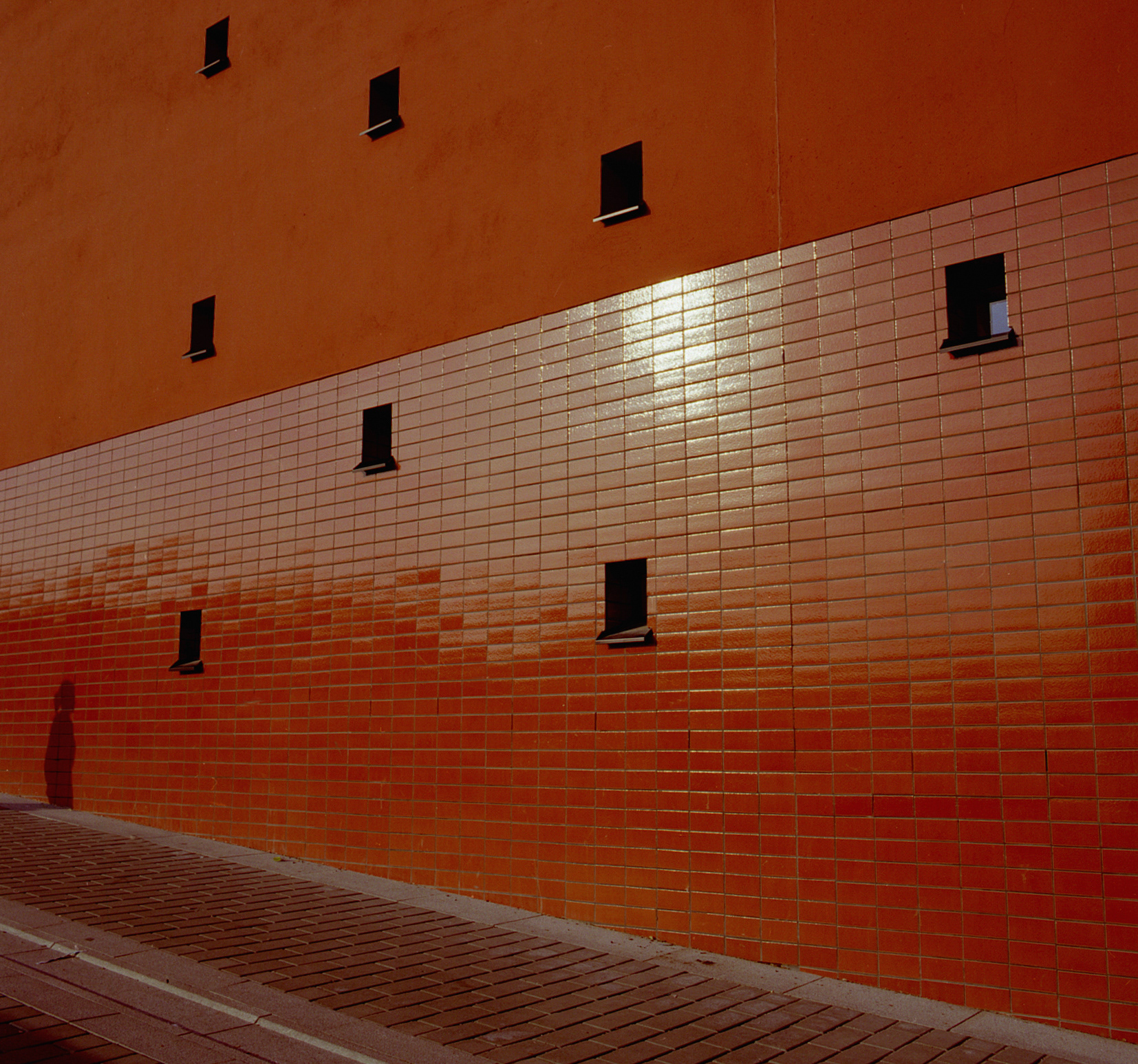 red wall with small windows with a shadow cast on it.
