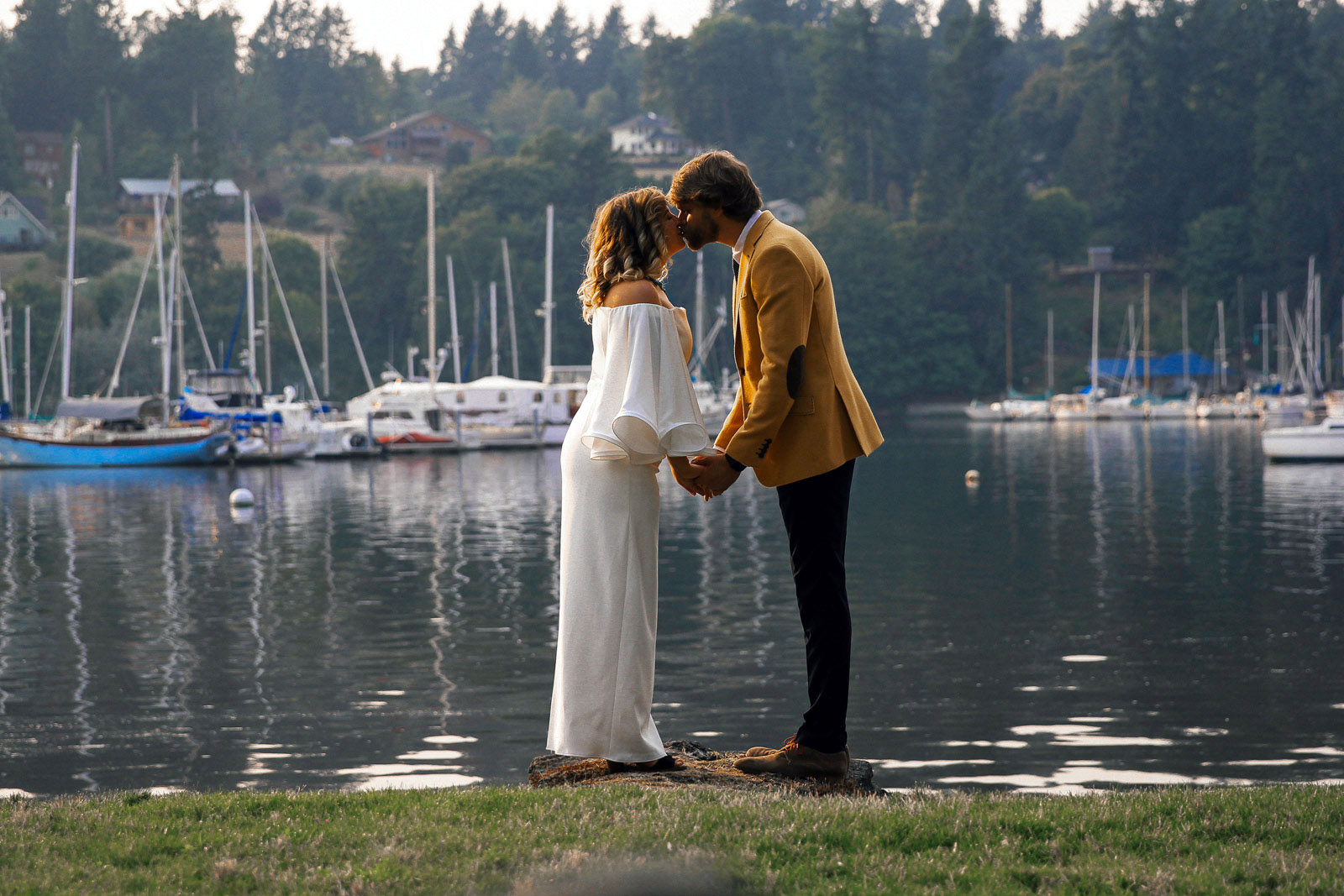 Couple kissing at water's edge, Washington state lake and sailboats in background