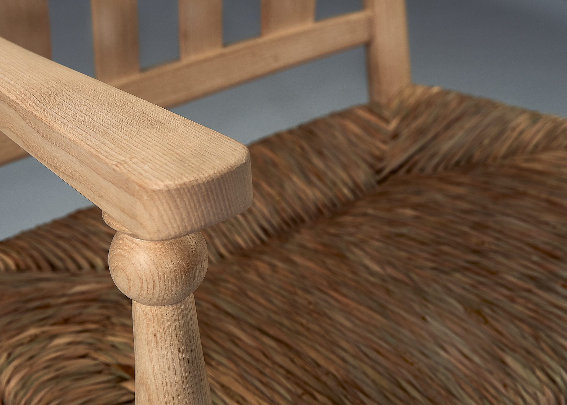 tight close up of a chair made of ash, a light-coloured wood, with its natural rush seat in the background