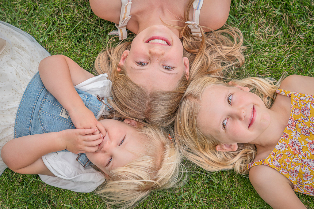Family picture of three young girls laying in the grass. Shot by Scott Campbell Photography MT