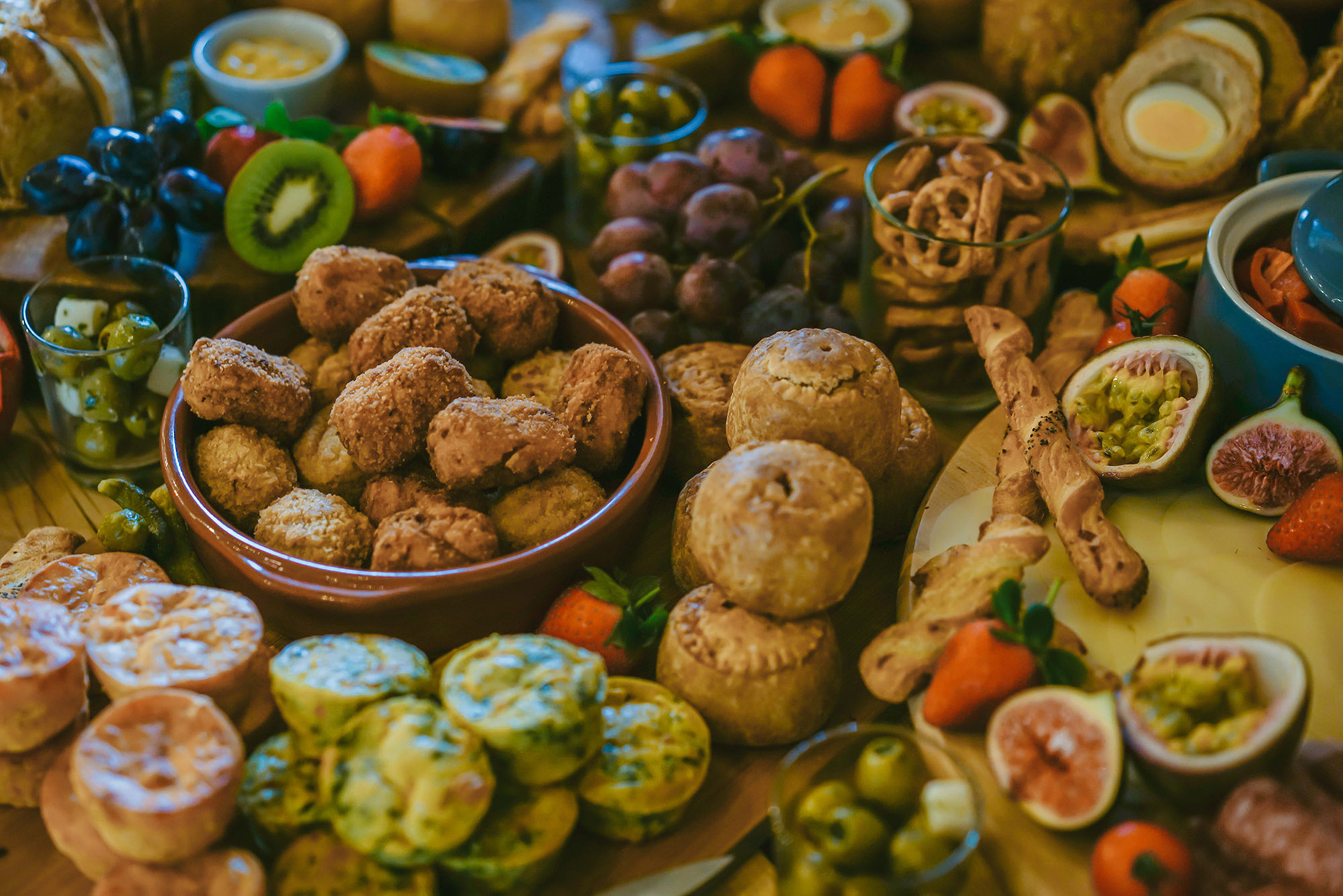 warm and colourful display of pork pies chicken bites grapes strawberries and kiwis on wooden display table at candid country barn wedding
