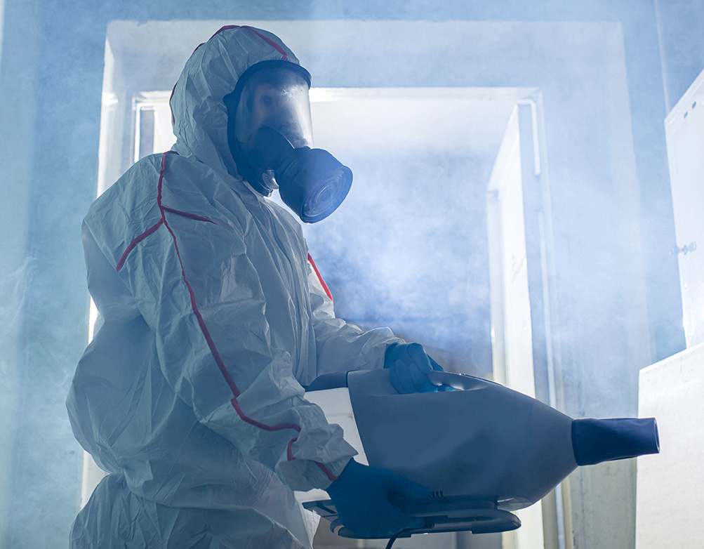 Guy in hazmat suit using a fogging machine to spray a space