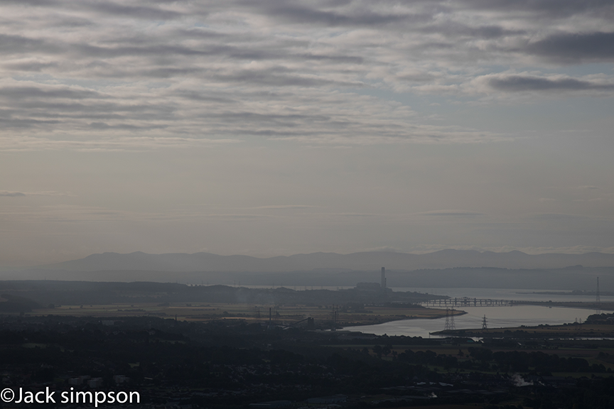 This rather atmospheric image was taken from the summit of Dumyat, which is the most westerly top of the Ochil Hills. As you can see it was a rather hazy morning with a very fine mist covering the estuary of the River Forth. In the centre of the image are the two bridges that span the forth at the village of Kincardine which is situate to the fore of the chimney stack of Longannet Power Station the distance from where the photo was taken is approx 12 miles away.
