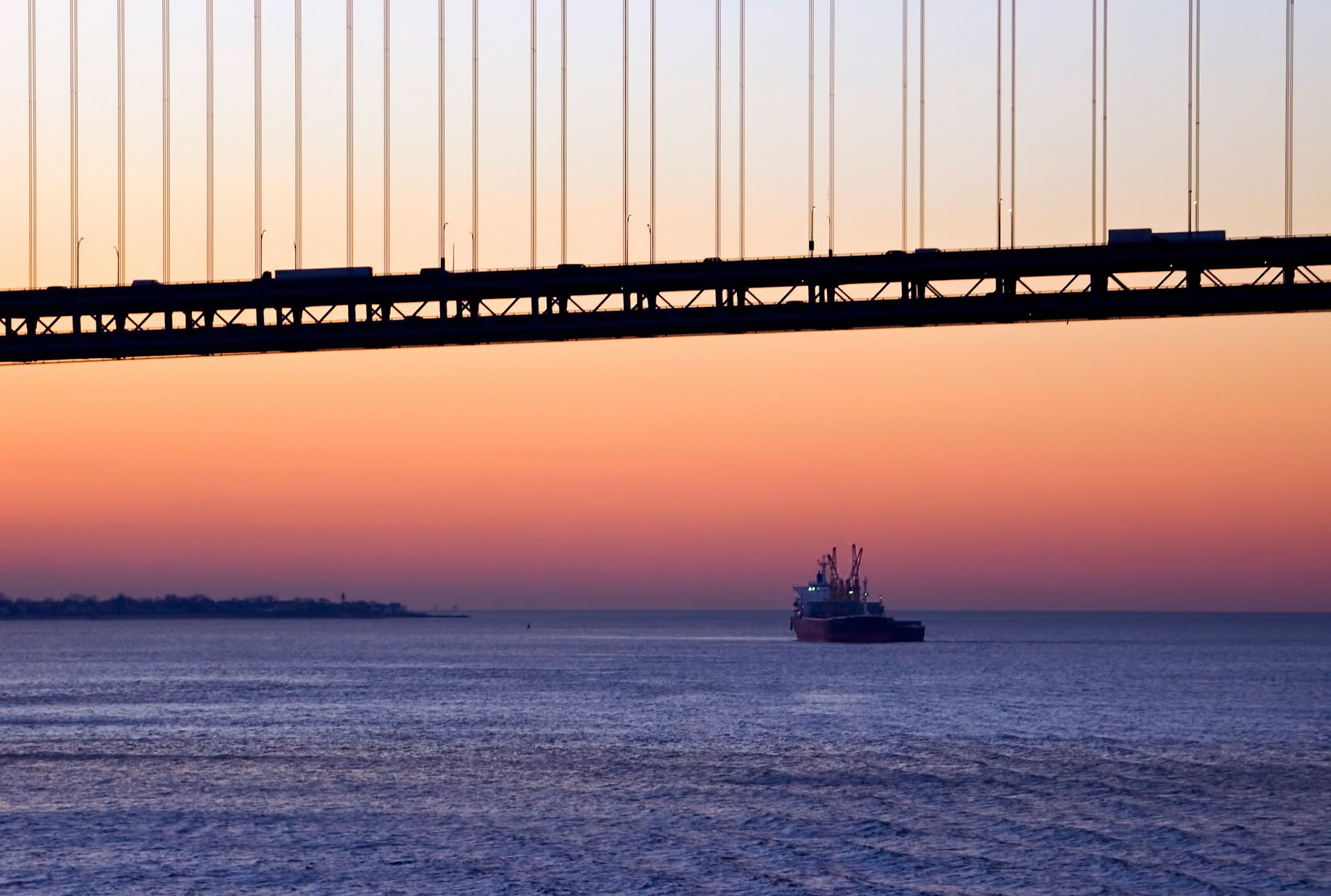 A boat heads away from New York City under the Verrazano Narrows Bridge at dawn.
