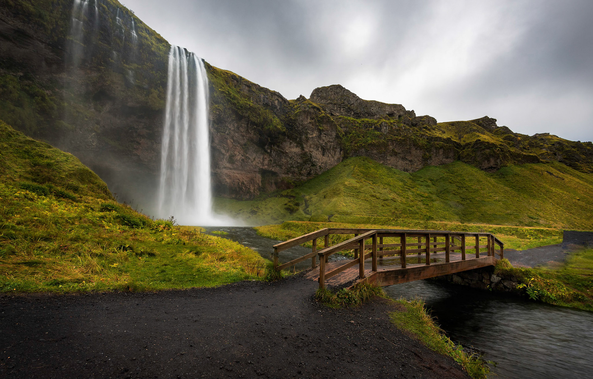 Seljalandfoss This waterfall has to be one of my favorites that I was able to photograph in Iceland! The fact that you are able to walk behind this waterfall made this beast truly special ! Before visiting this, I had imagined, climbing up the slippery path to the cavern behind the waterfall, and the sun would be rising through the mists. Unfortunately it was overcast and cloudy when we visited it. Still it was an experience to photograph this early morning in chilling winds soaked to the bones from the water mist. You get to a point where you just are going through the motions, sheer will making you cover all the possible compositions when your mind is screaming at you to get indoors into warmth and dry off. This was one of the easier shots of that morning, standing back from the waterfall away from the spray, admiring the magnificent waterfall in all its glory.