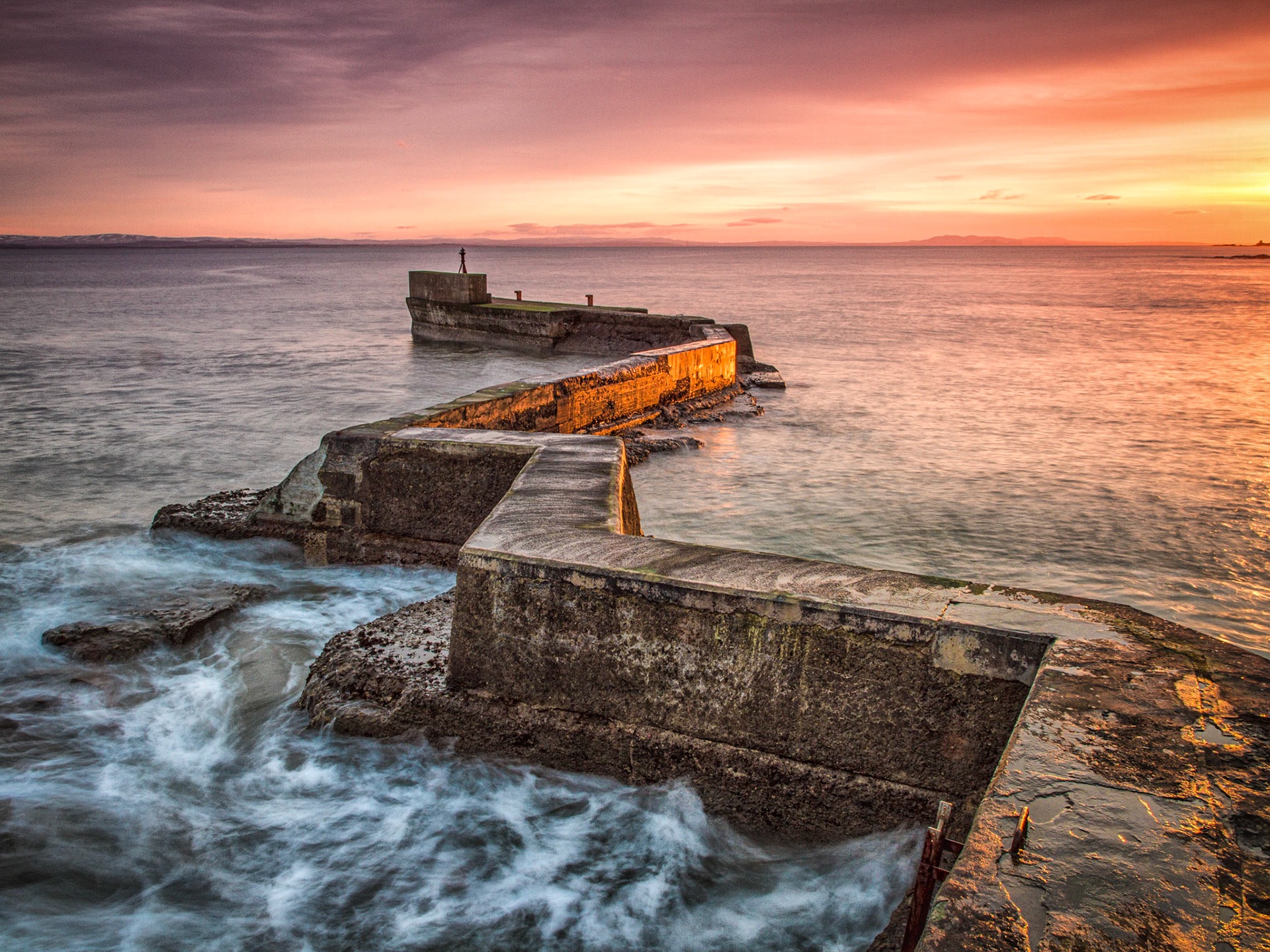 The breakwater at the mouth of St Monans harbour in Fife. What struck me was the glow of the setting sun on the calm waters of the leeward side of the breakwater contrasting with the breaking waves on the windward side.