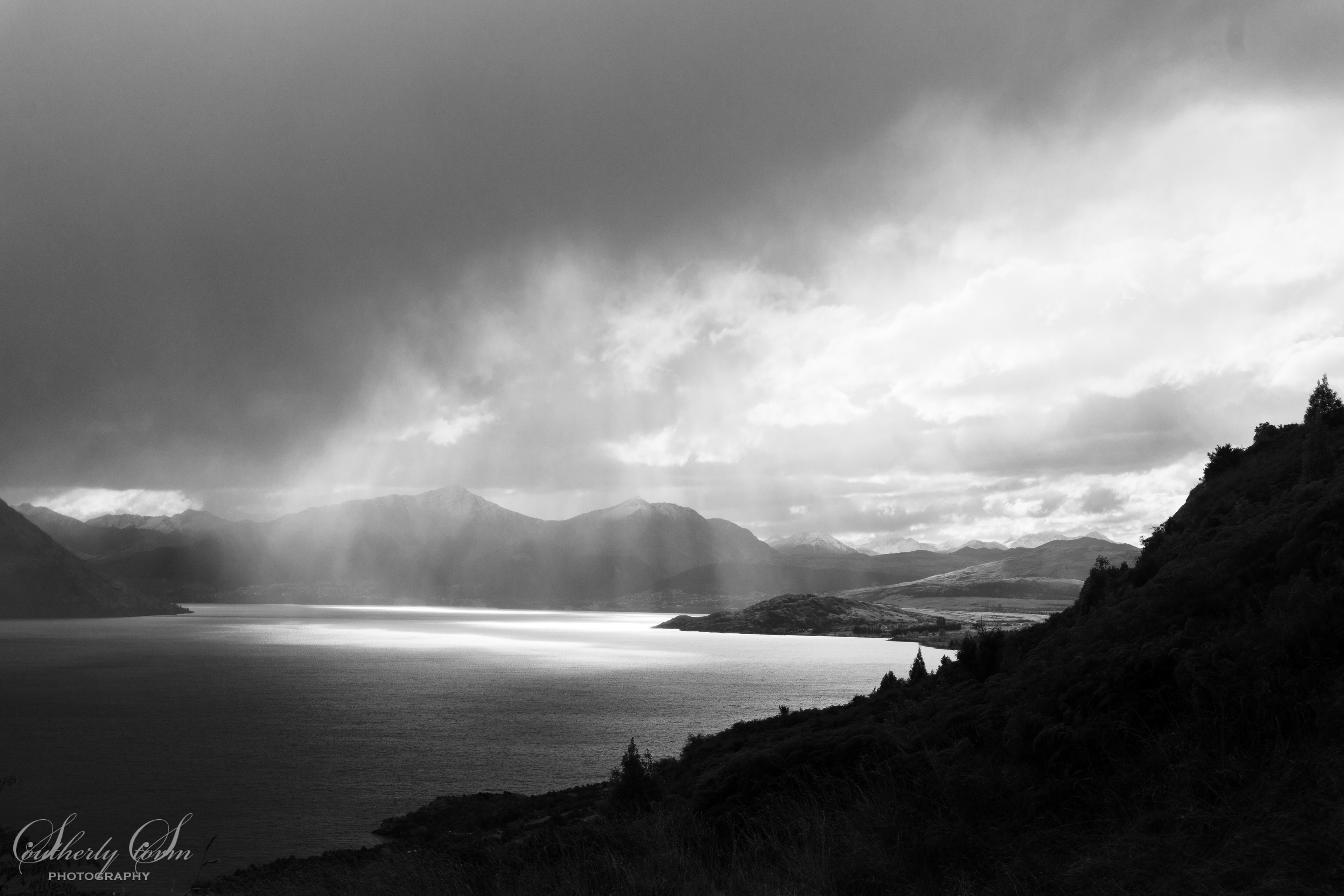 Black and white of storm clouds and sun fingers over Lake Wakatipu