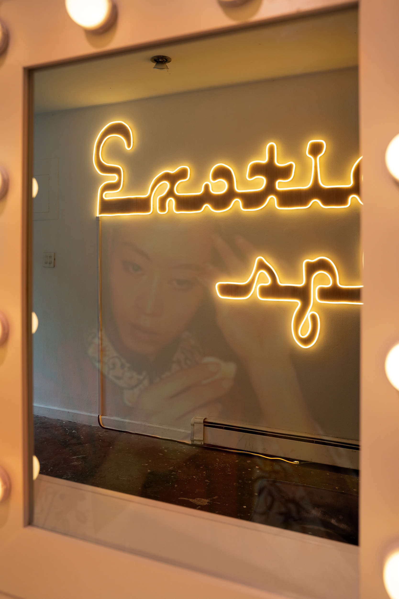A reflection of a person and a neon sign in a vanity mirror