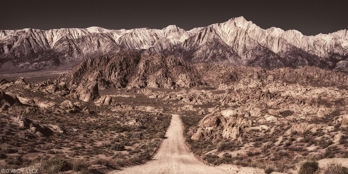 Dirt road heads towards the Sierra Nevada Mountains as it traverses through the rocks of the Alabama Hills, California
