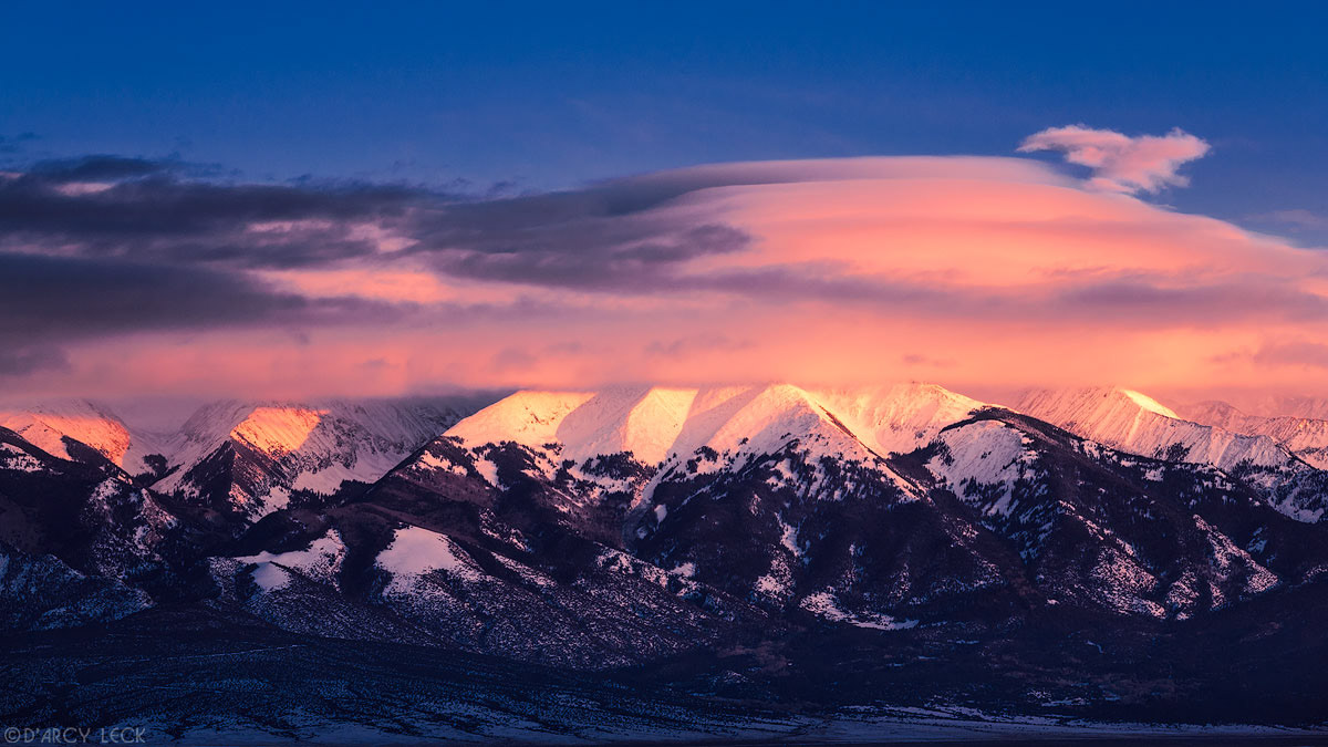 Lenticular clouds cap the snowy Blanca Peak and the Sangre de Cristo Mountains at sunset as they rise above the San Luis Valley in winter, Colorado