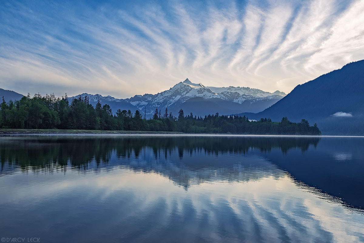 Mount Shuksan and cirrus clouds catch morning sunrise light and reflect in Baker Lake, Washington
