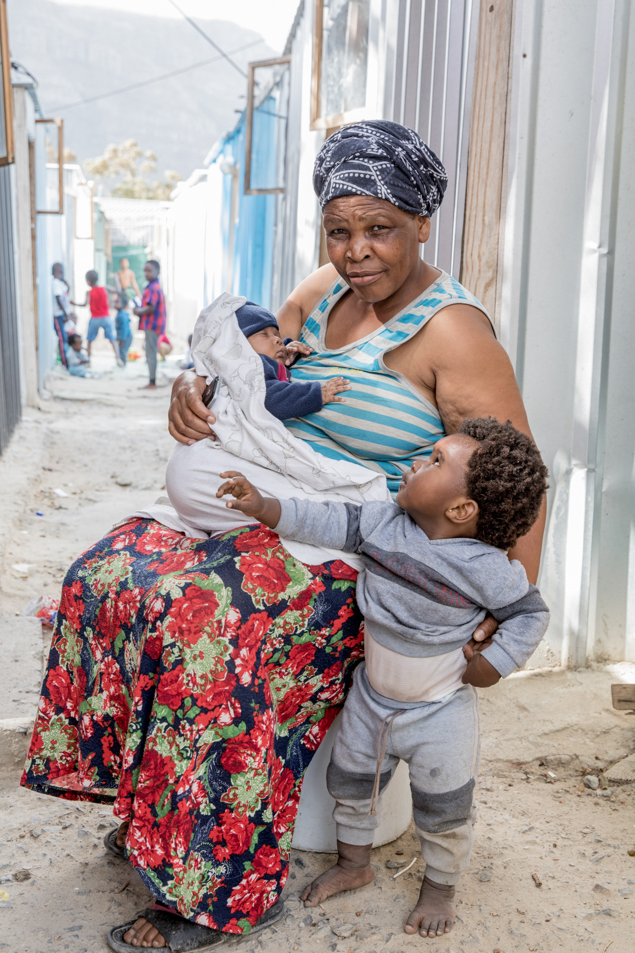 Nonstapo Maqabuka with infant granddaughter Alunamda and grandson Inako outside the 3x6 meter home she shares with her grandchildren and daughter.