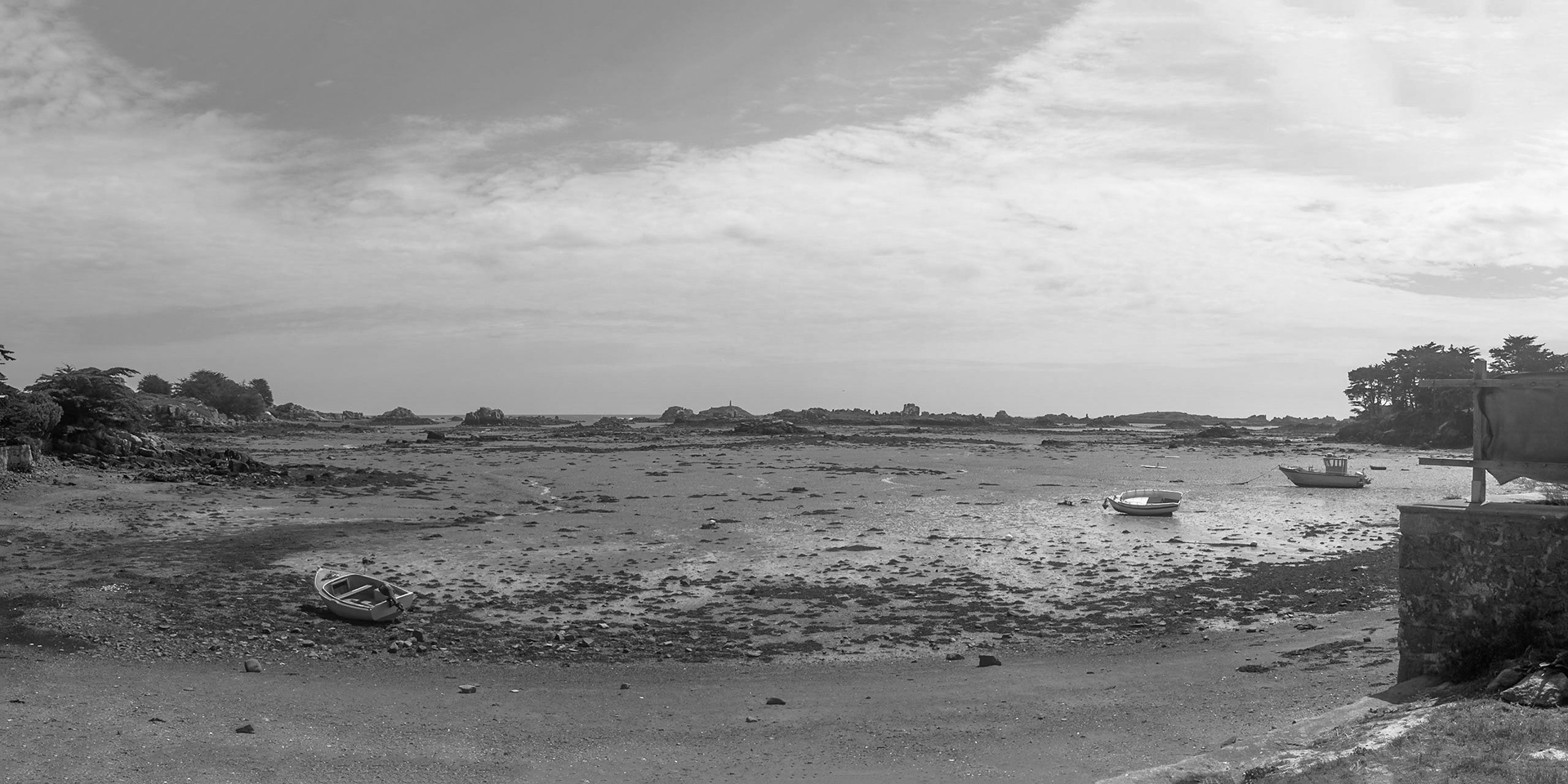 Black and white image of a bay at low tide on Ile de Bréhat, Bretagne, seen from the D104 near Les Brises. Almost mid-image one sees a pike on one of the very small islets that litter the coast. Google Maps labels that as Roc'h Louet, but we think this is incorrect.