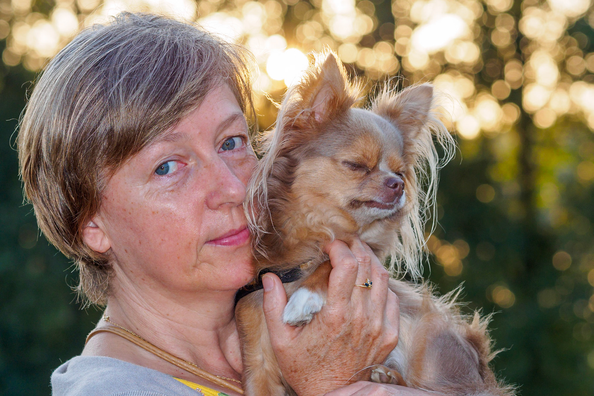 Friendly Lady with dreaming Chihuahua against a sunlit forest