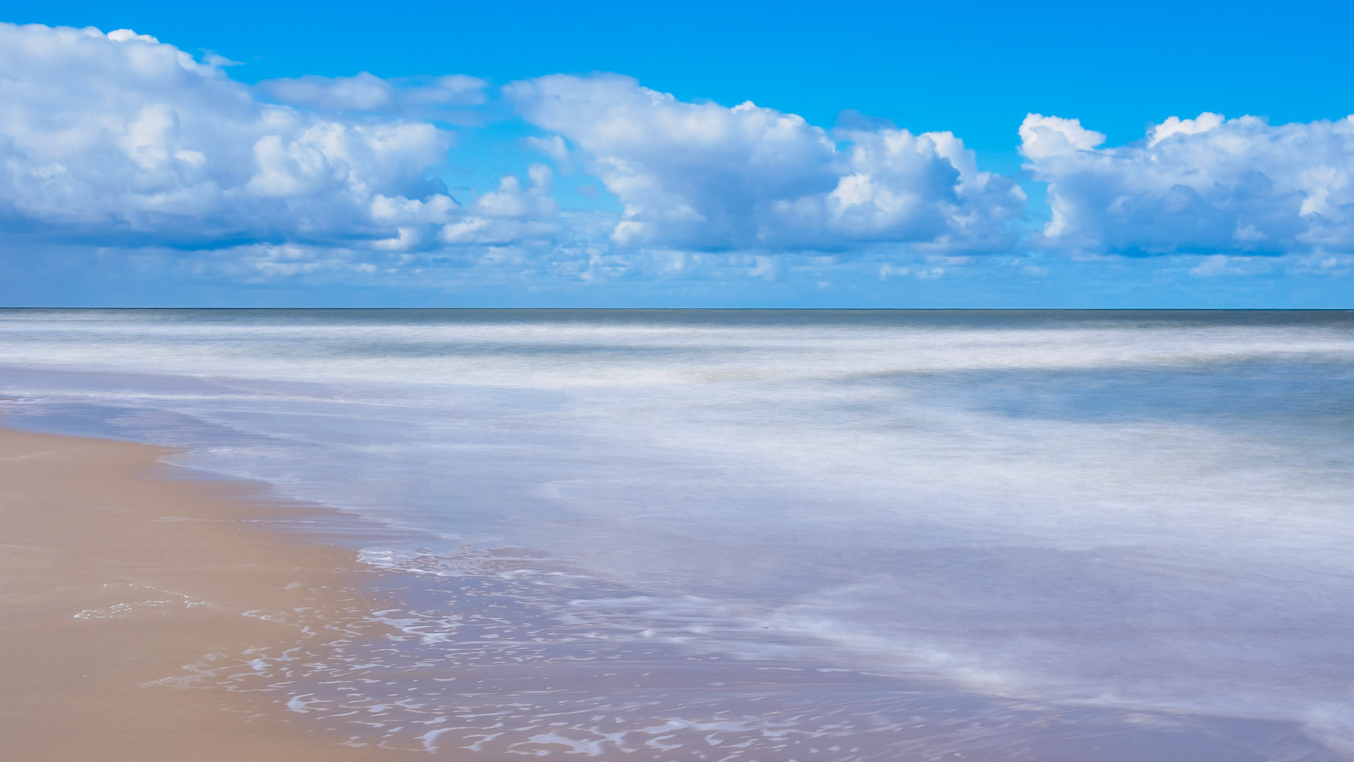 Long exposure of the North Sea under a cloud-rich blue sky