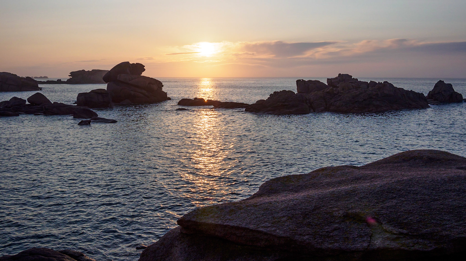 The slightly veiled sun setting over the English Channel at Ploumanach, France, reflecting in the water,  casting a soft dim light over the pink granite rocks. As it happened, the rays of light from the sun got caught in a small opening in the rocks causing a starburst effect as if there was a lens there just for us.