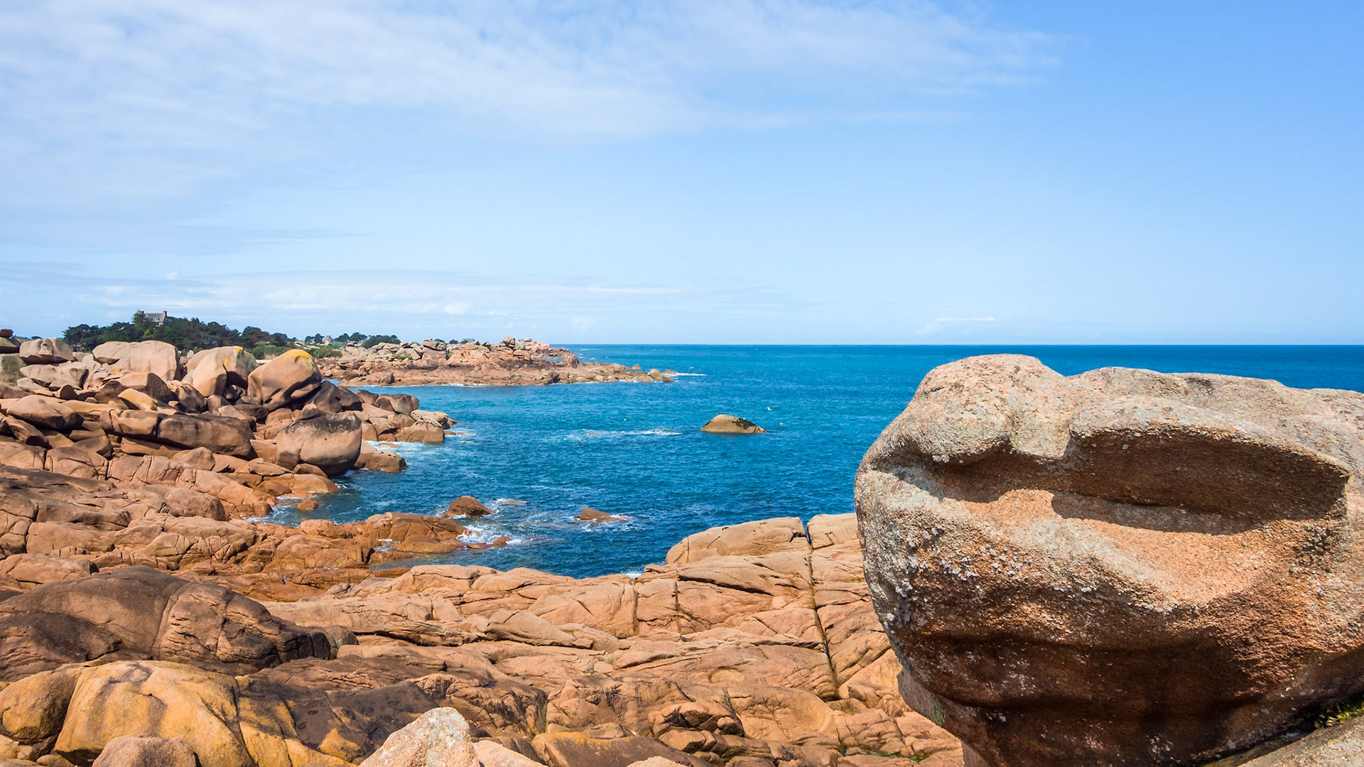 Pink granite boulders on the coast of Brittany, France. In the background the castle of Costaérès.