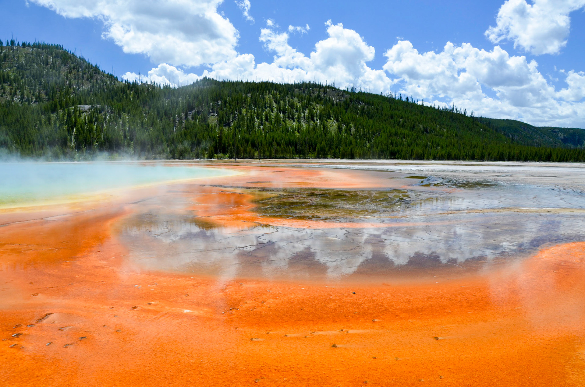 Cloud reflections and steam rising above the bright colors of Grand Prismatic Spring