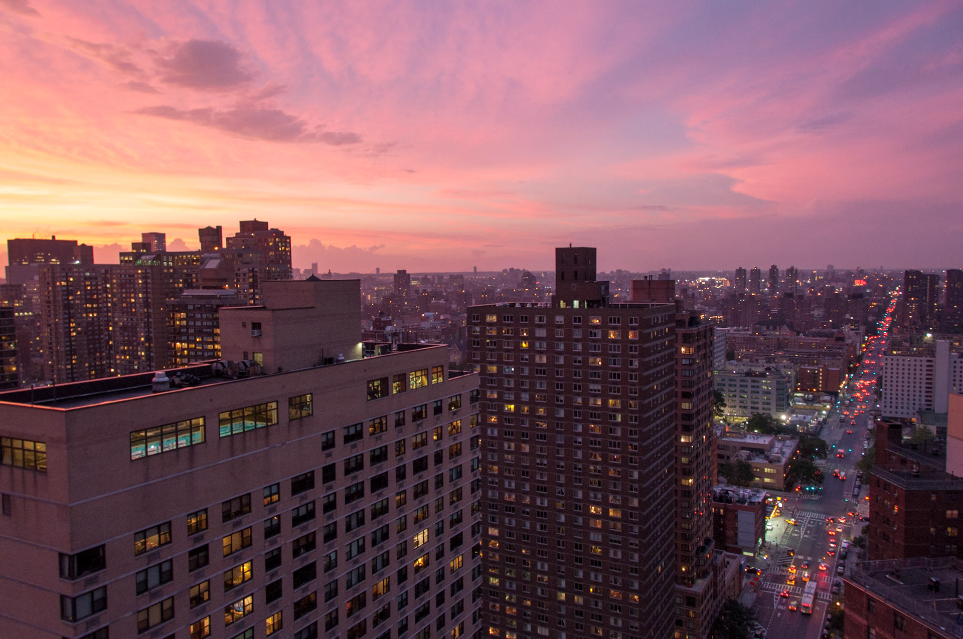 The sun sets over Harlem and the Bronx.  The George Washington Bridge is in the distance to the right.  Yankee Stadium and the History Channel sign are visible in the Bronx.